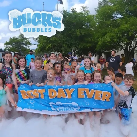 Campers covered in foam holding a Bucks Bubbles Best Day Ever banner